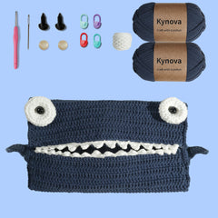 Crochet kit for making a shark-themed storage bag, including navy yarn, a crochet hook, buttons, a sewing needle, and a video tutorial.