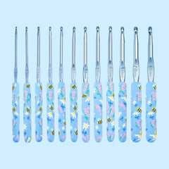 A set of 12 crochet hooks with floral patterned handles in various sizes, laid out in a row against a light blue background.