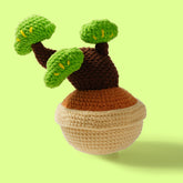 A handcrafted crochet tree with cloud-shaped leaves in green and brown colors, on a beige spherical base, against a light green background.