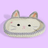 A handcrafted, crochet kitty eyeglass case designed to resemble a cat's face with ears on top, made in beige, white, and gray colors.